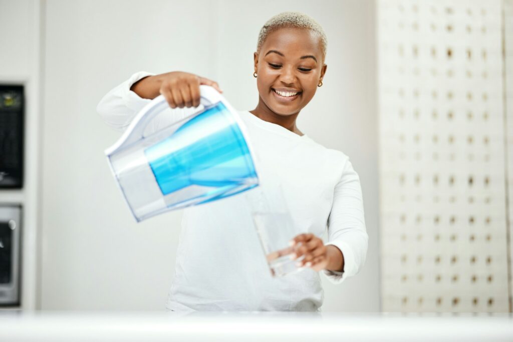 Black woman, pitcher and glass with water filter for clean and fresh purification at home. Happy fe