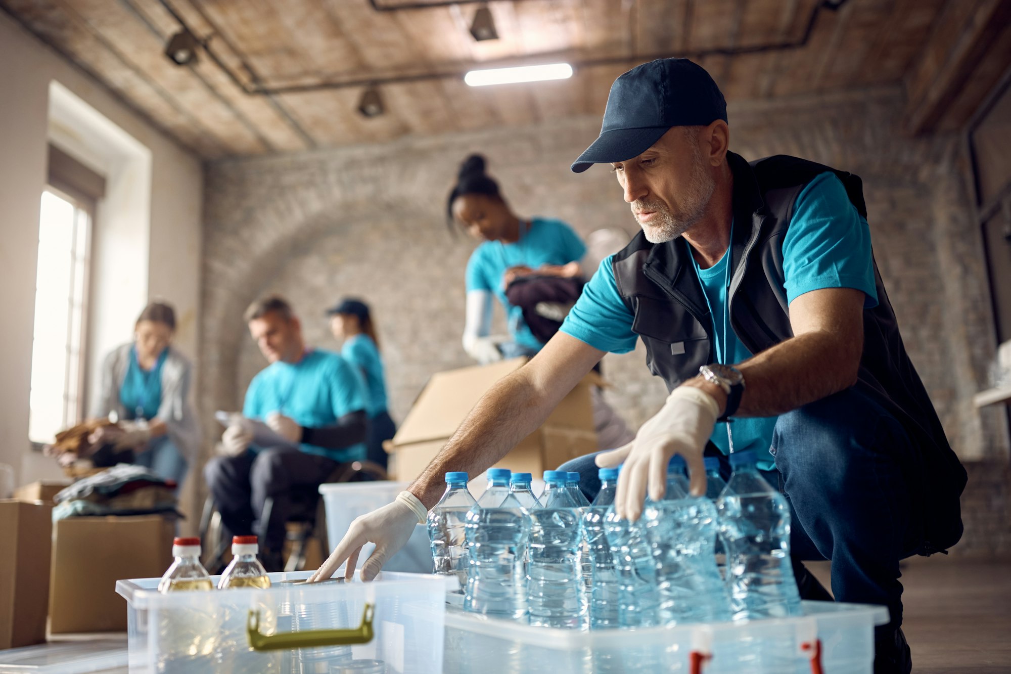 Mature volunteer organizing donations in boxes while working at humanitarian aid center.